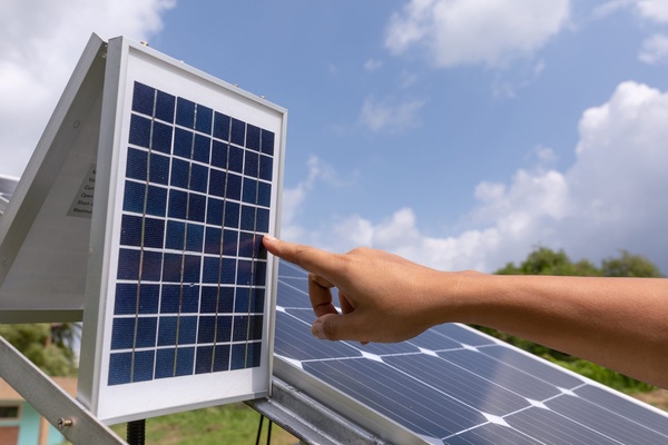 Main désignant un petit panneau solaire devant un champ photovoltaïque