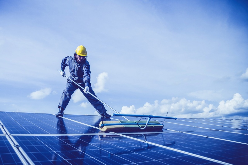 Technicien en combinaison nettoyant des panneaux solaires à la raclette