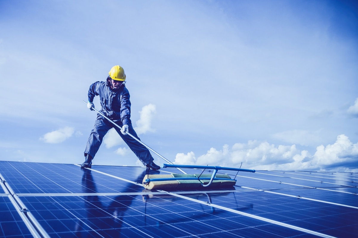 Technicien en combinaison nettoyant des panneaux solaires à la raclette