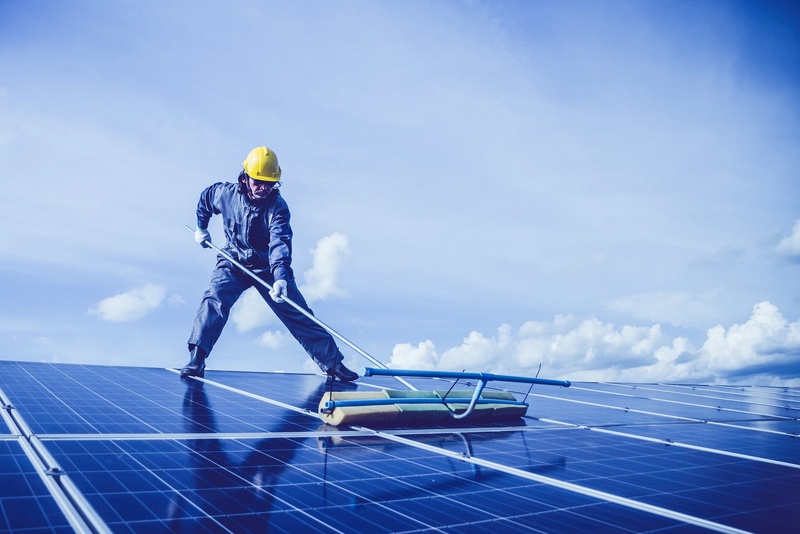 Technicien en combinaison nettoyant des panneaux solaires à la raclette